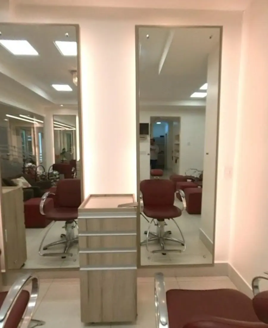 Estações de atendimento com espelhos altos iluminados e cadeiras bordô