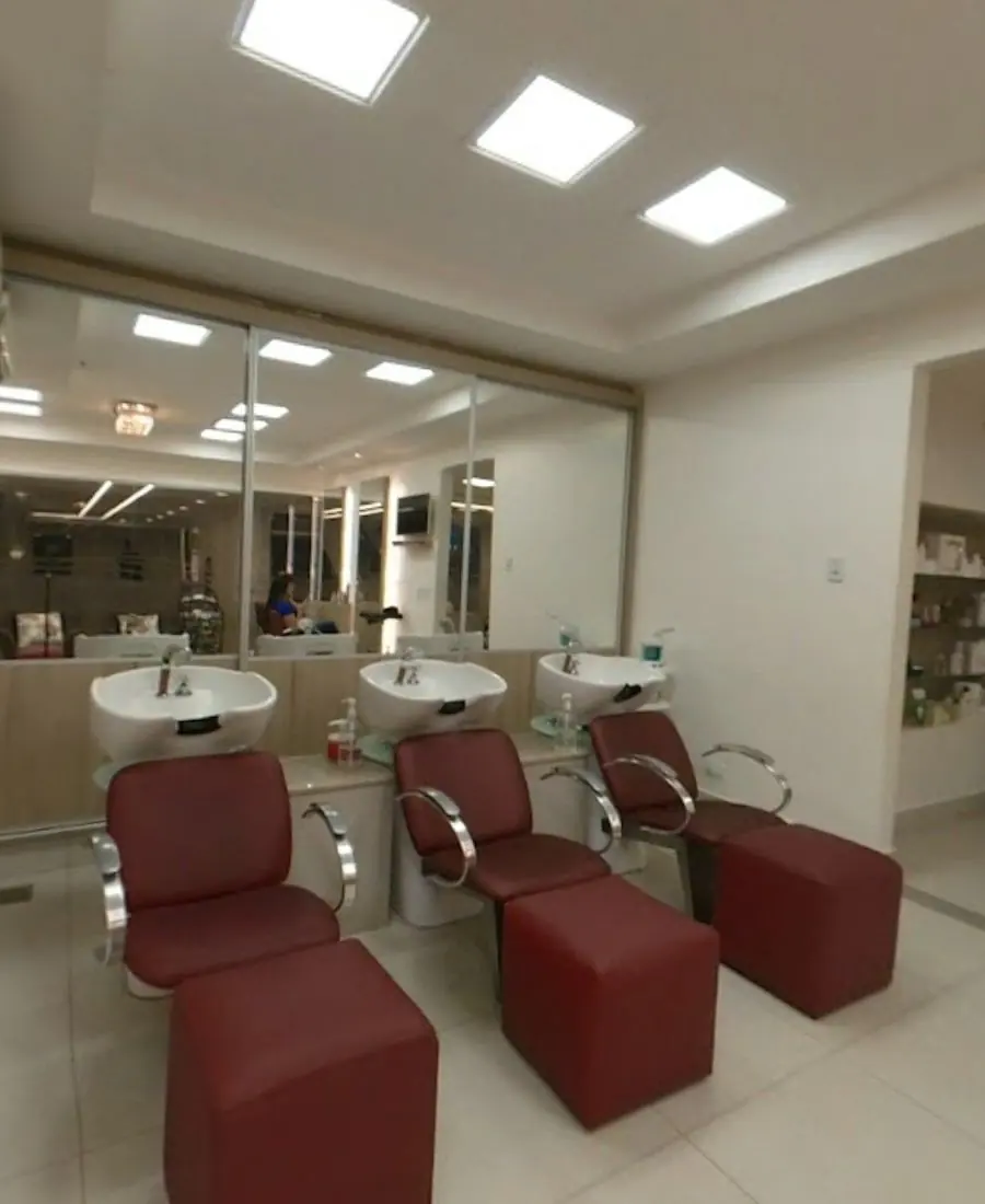 Área de lavagem com três lavatórios brancos, poltronas bordô e apoio para as pernas