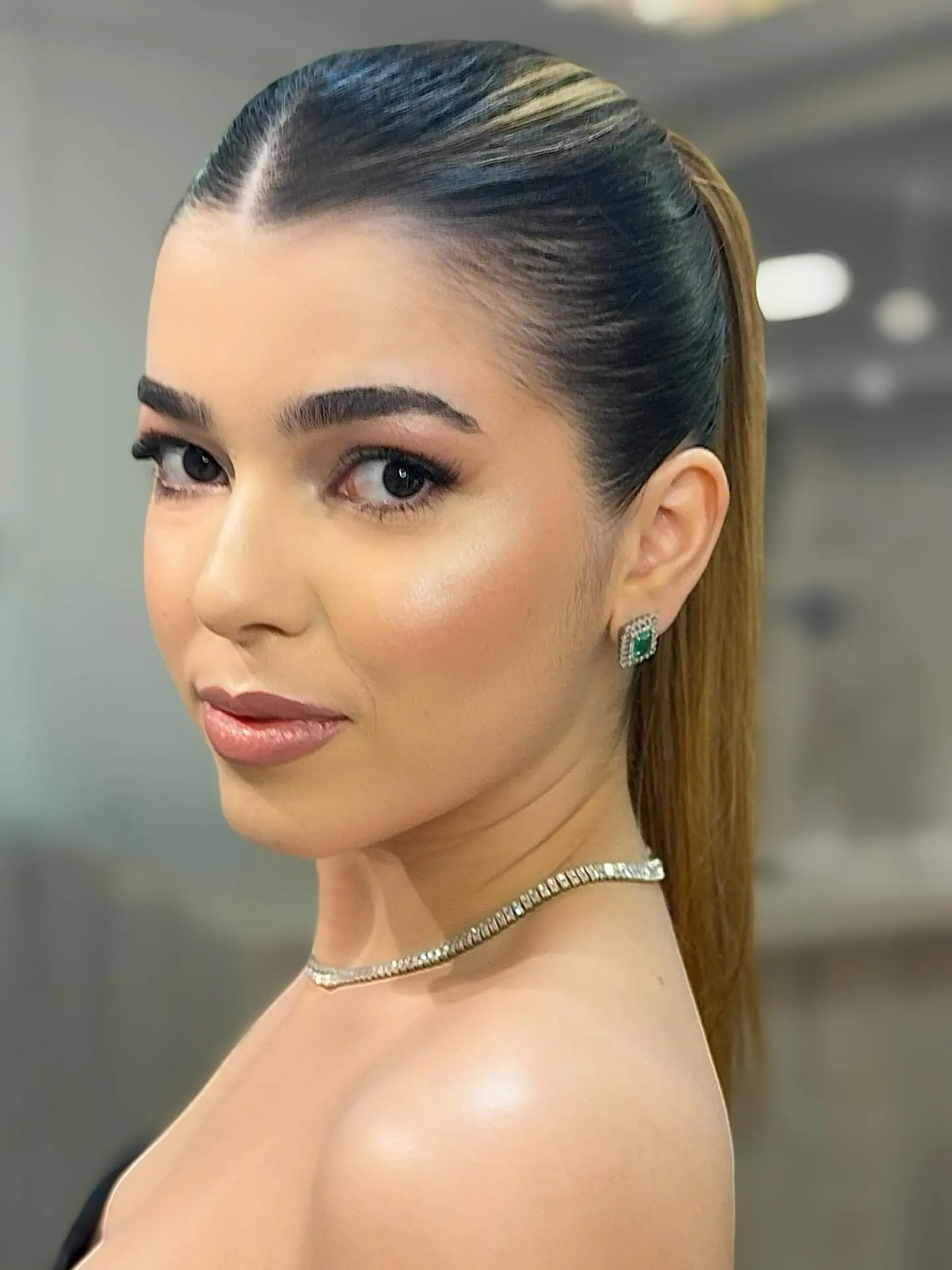 Modelo de perfil com rabo de cavalo polido e maquiagem iluminada, produzida no Studio Nill