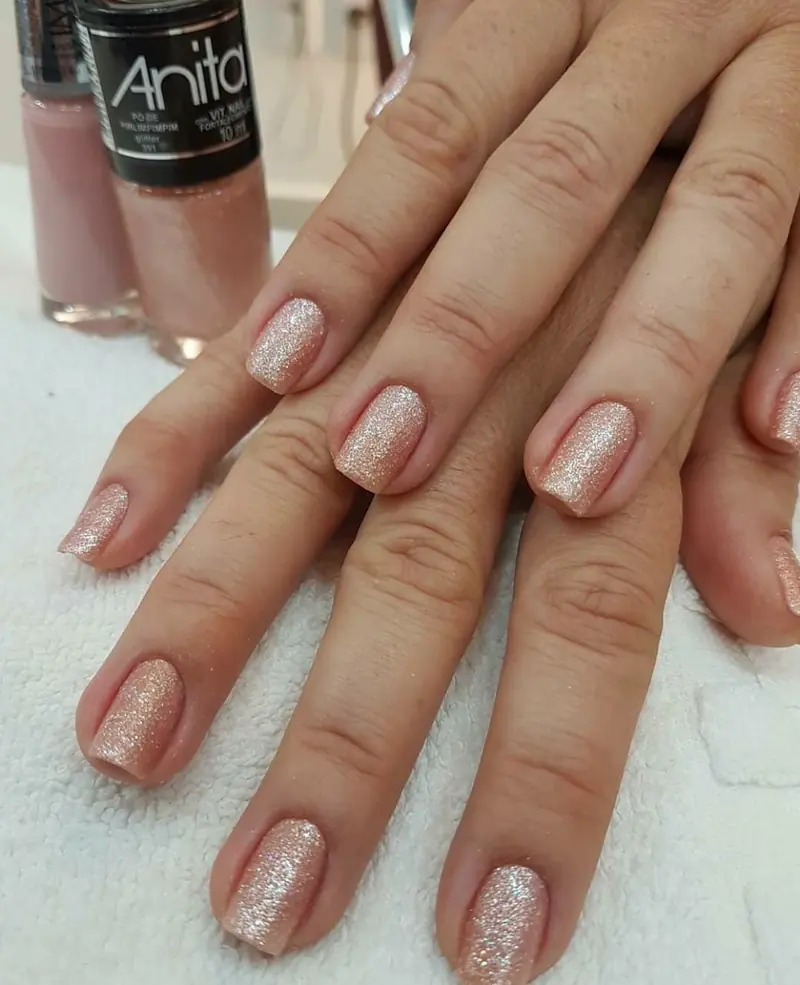 Unhas curtas com esmalte nude cintilante, ao lado dos vidros de esmalte