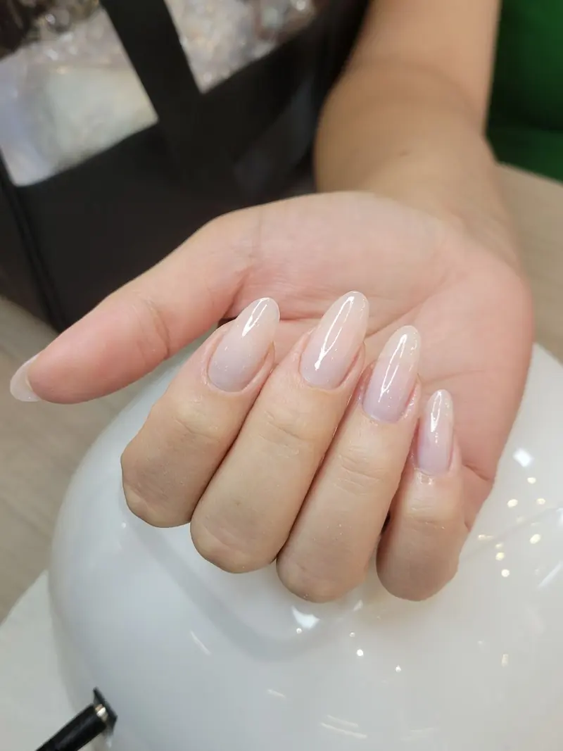 Unhas amendoadas em tom nude rosado, com a mão apoiada sobre a cabine de secagem